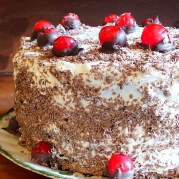 Black forest cake with chocolate covered cherries on it.