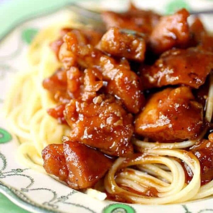 Cubes of chicken covered in a tangy sauce over spaghetti.