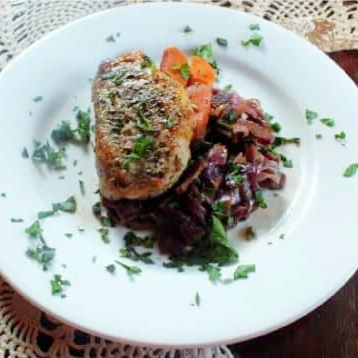 Golded brown braised pork and red cabbage on a white plate.