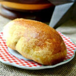 A golden brown cornmeal sandwich roll on a plate.