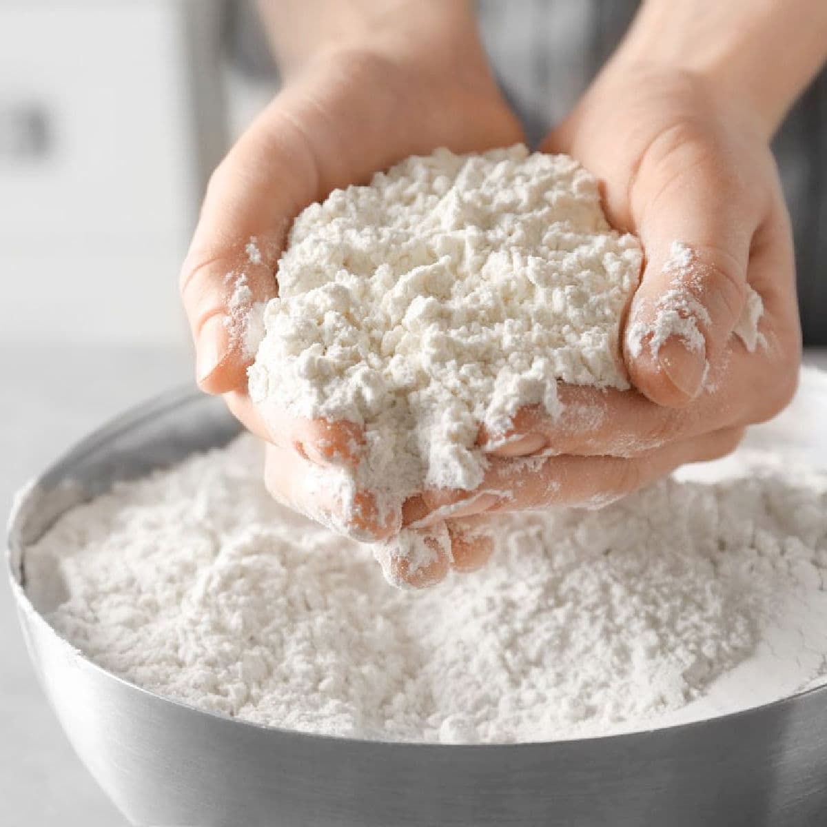 A woman's hands holding white flour above a bowl.