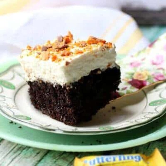A square of chocolate cake with whipped cream on top sprinkled with crushed  Butterfingers candy.