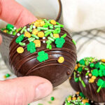 Hand holding an Irish Cream hot chocolate bomb. Text overlay for Pinterest.