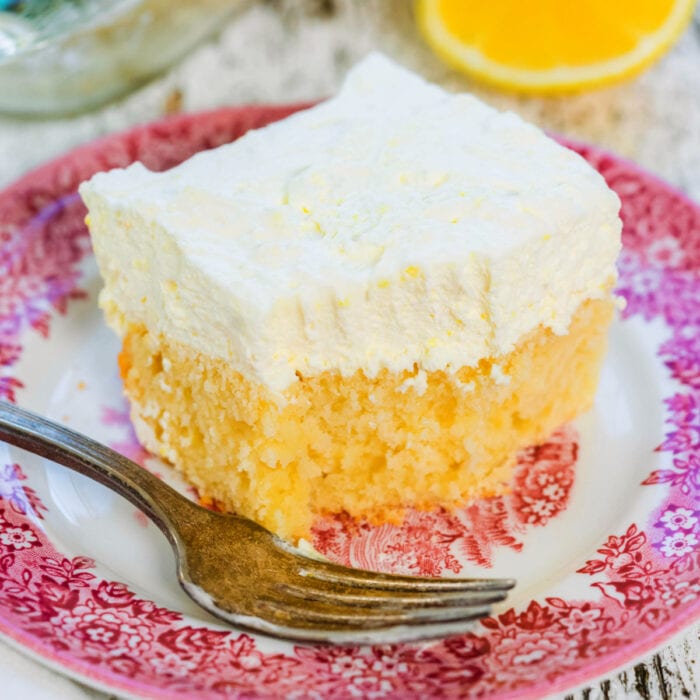 Square of lemon cream cake on a red and white plate.