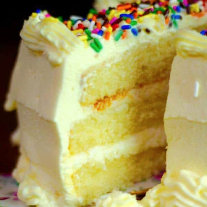 A triple layer lemon cake with whipped lemon buttercream frosting with a slice being removed.