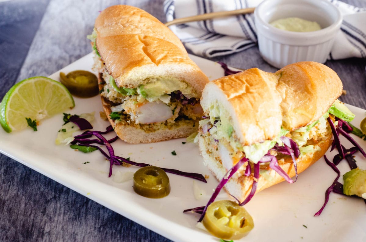 Fried shrimp po' boy sandwich cut in half on a plate.