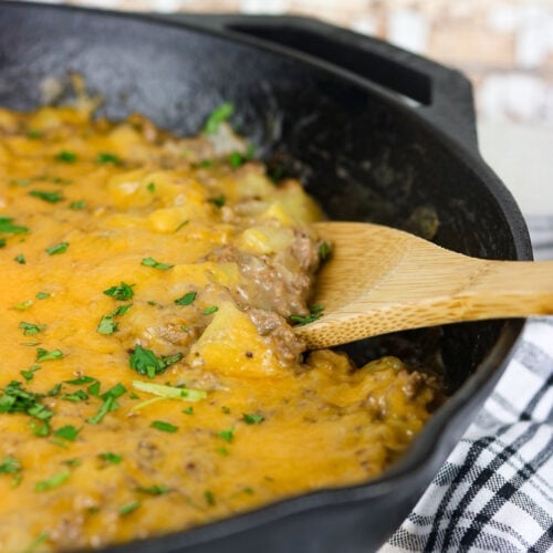 A wooden spoon serving a cheesy casserole from a skillet.