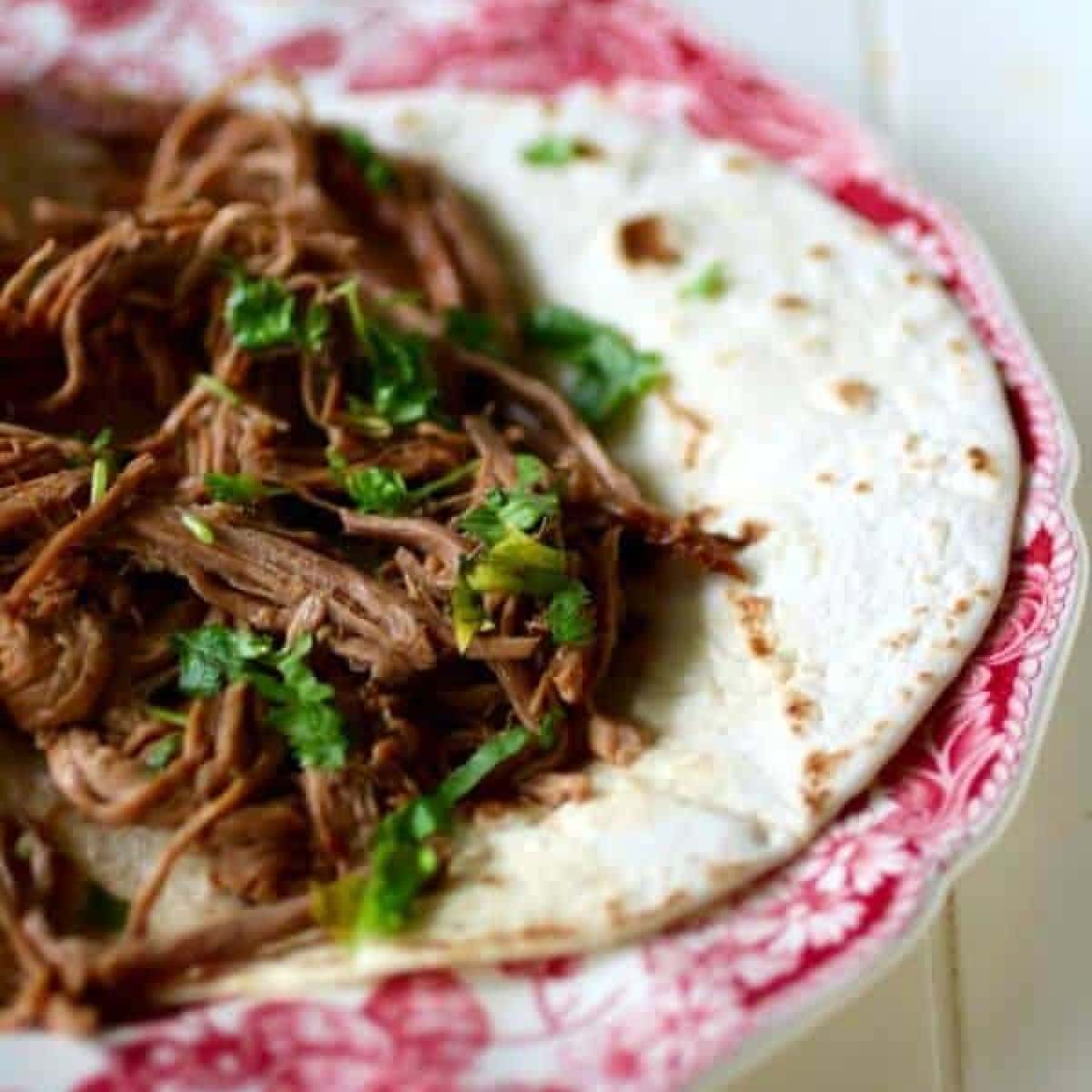 Shredded beef barbacoa on a tortilla.