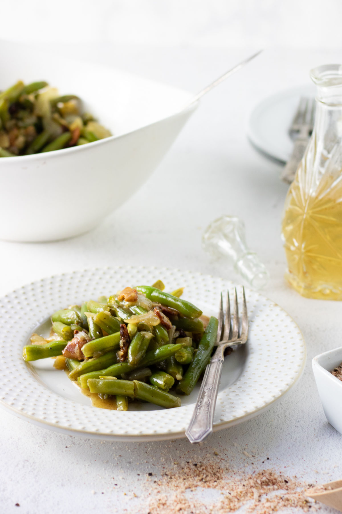 A plate of green beans on a table with the serving bowl in the background.