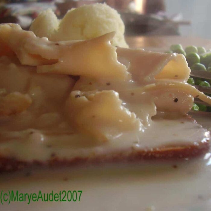 Slices of turkey stacked on white bread and covered with gravy.