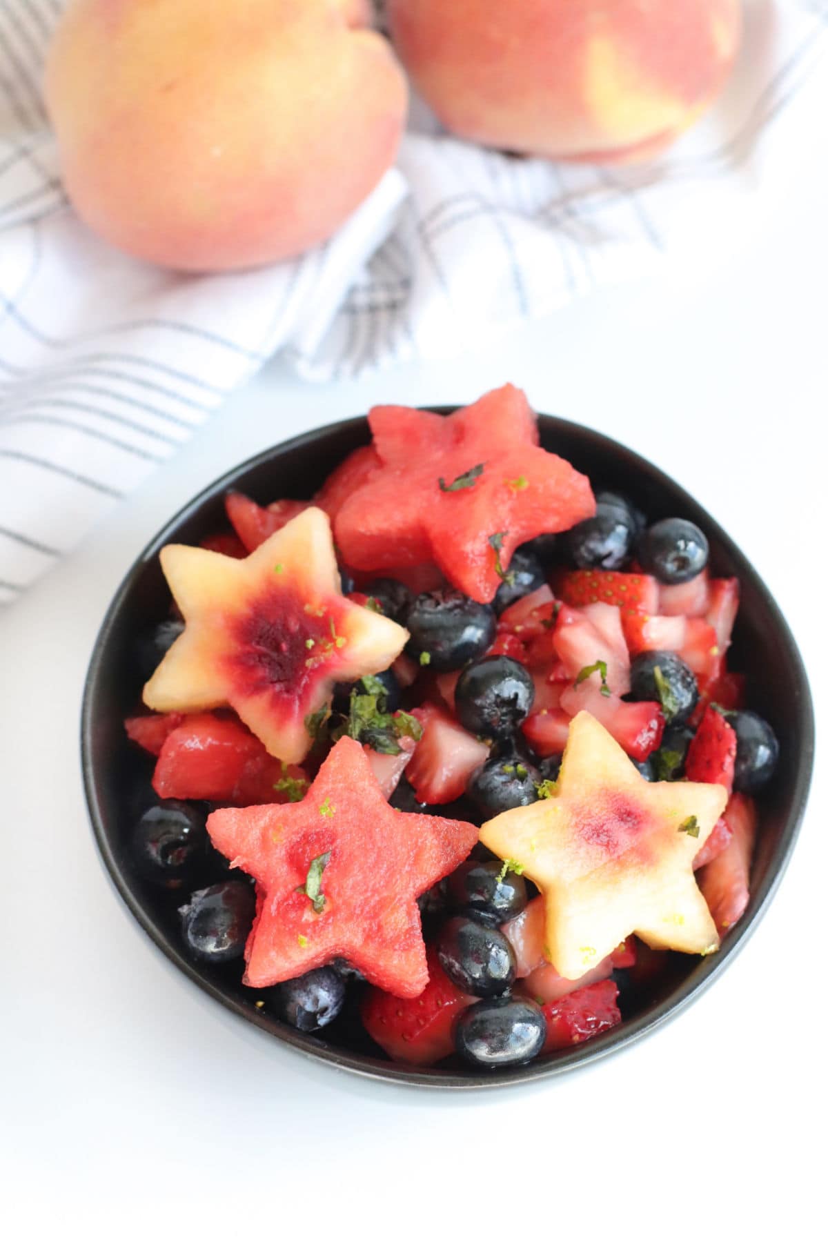 Overhead view of a bowl with watermelon and peach slices cut like stars and fresh blueberries.