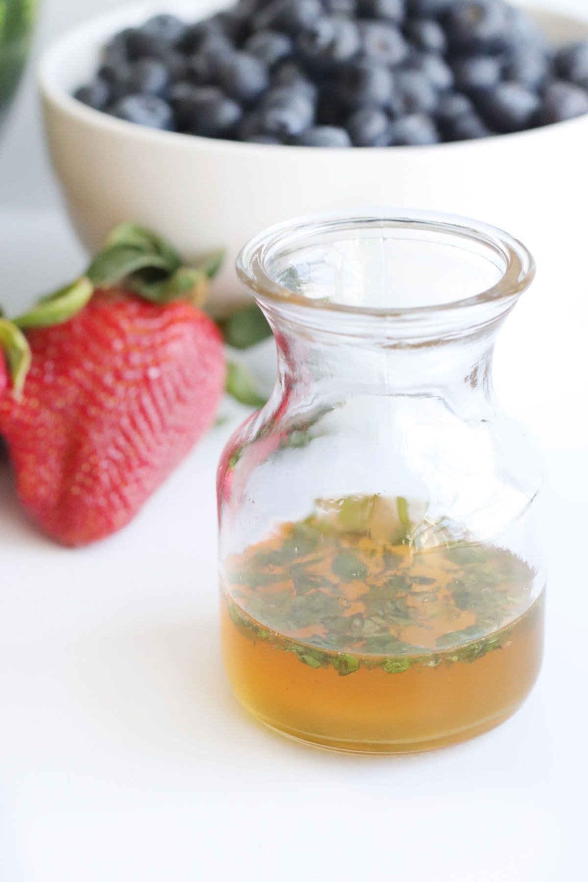 A bottle of homemade dressing sits in front of a bowl of blueberries.