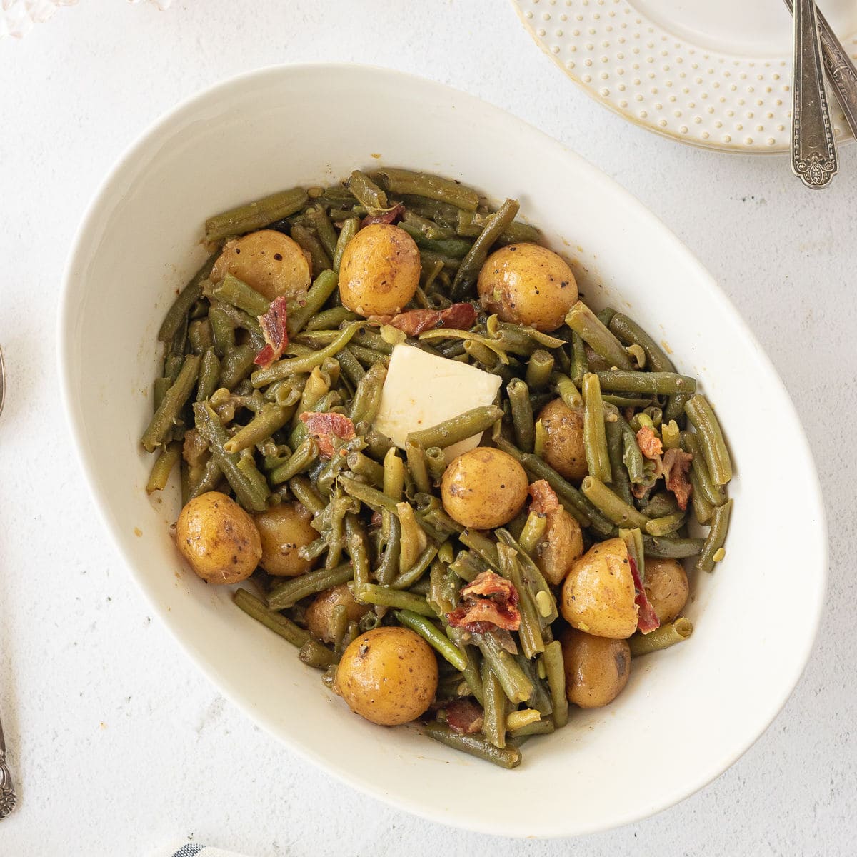 Overhead view of green beans and potatoes in a serving dish with a pat of butter melting on top.