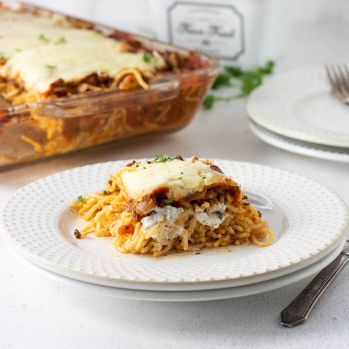 A serving of spaghetti casserole on a white plate with the casserole dish in the background.