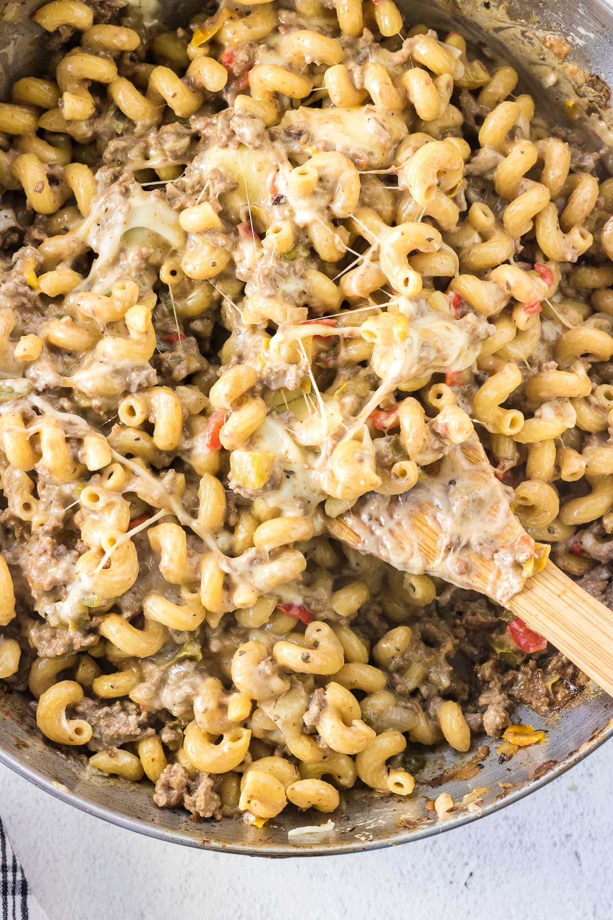 Overhead view of a pan of pasta with a wooden spoon in it showing the gooey, cheesy top.