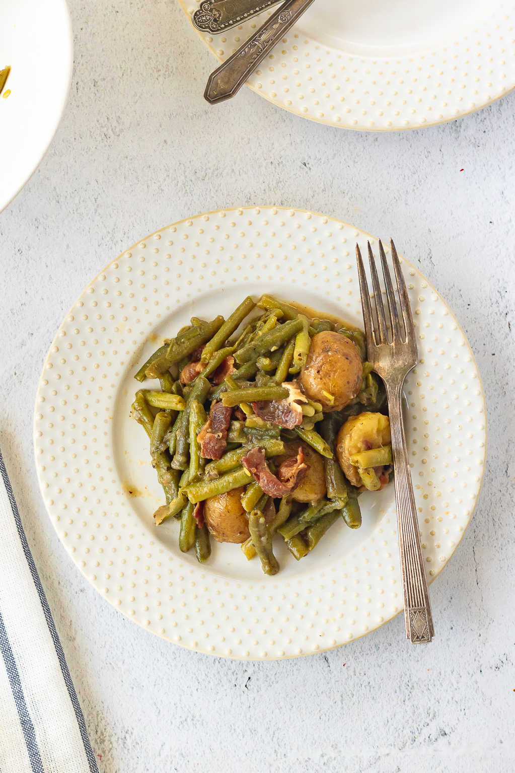 An overhead view of a serving of green beans and potatoes on a white plate.