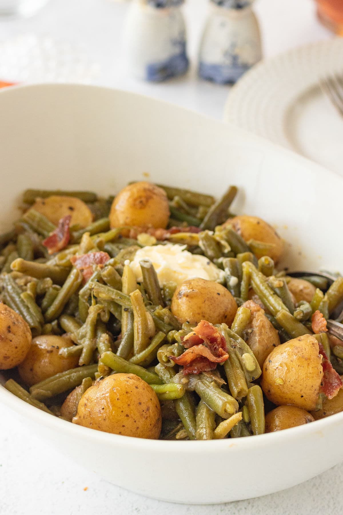 Closeup of a serving dish with cooked green beans and tender new potatoes in it.