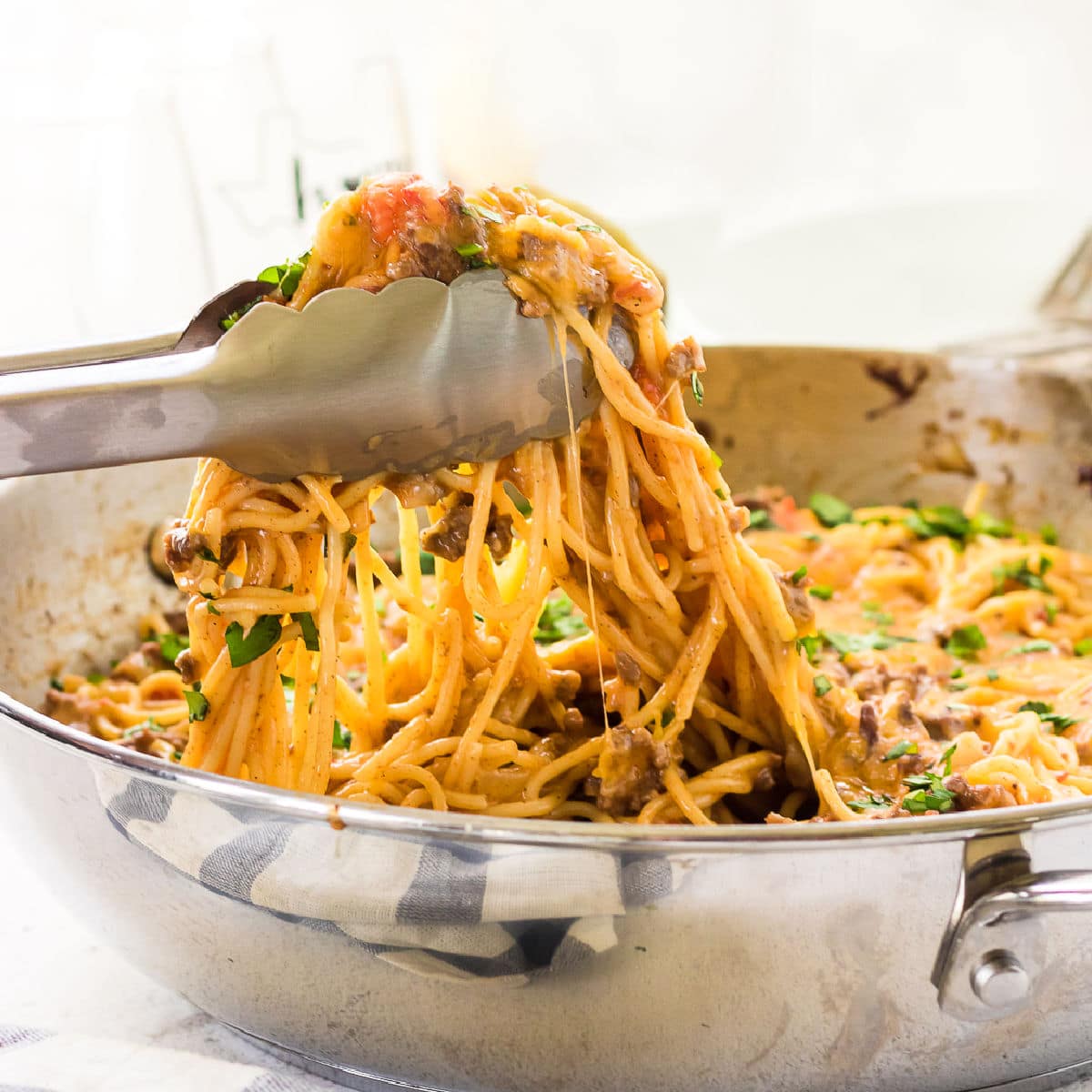 A closeup of tongs lifting a serving of taco spaghetti out of the pan.