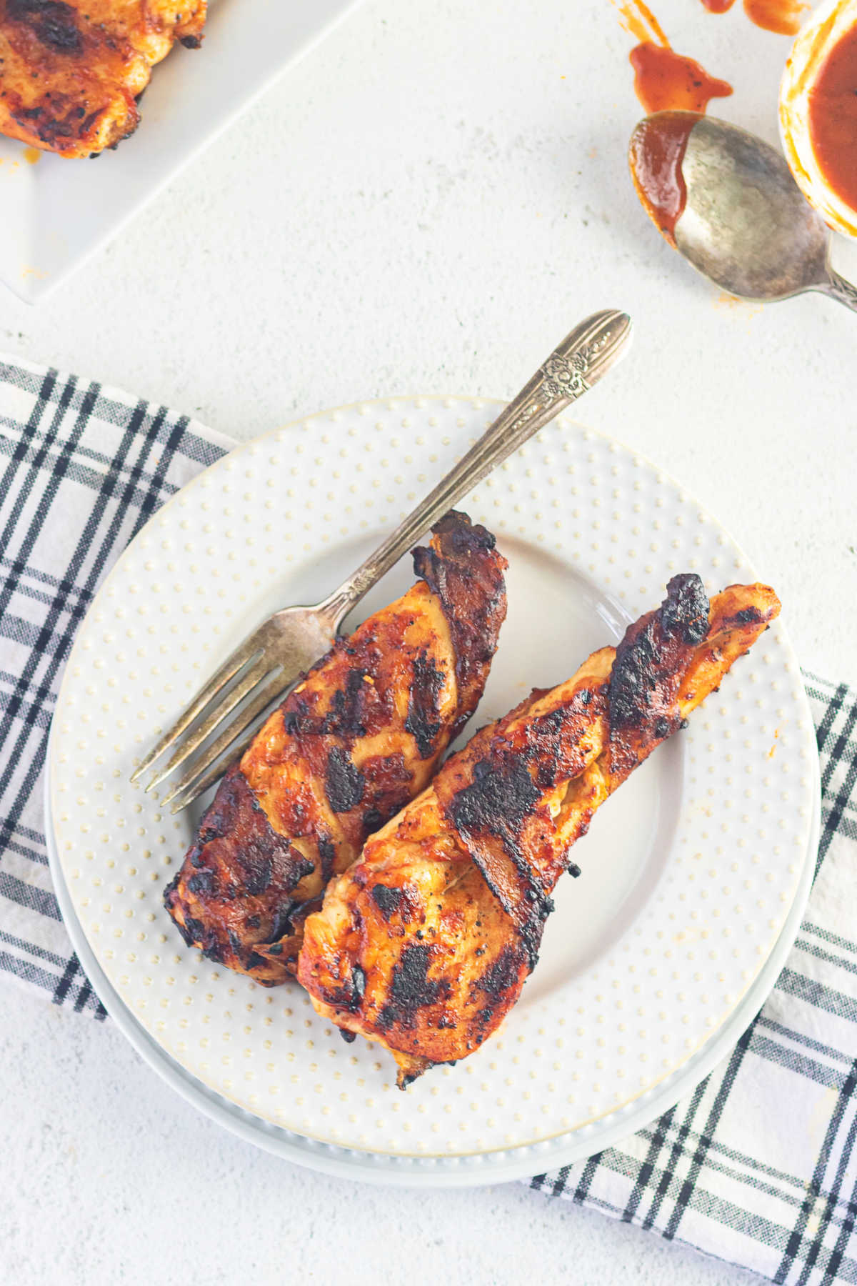 Overhead view of two pieces of cooked chicken breast on a white plate with barbeque sauce in the background.