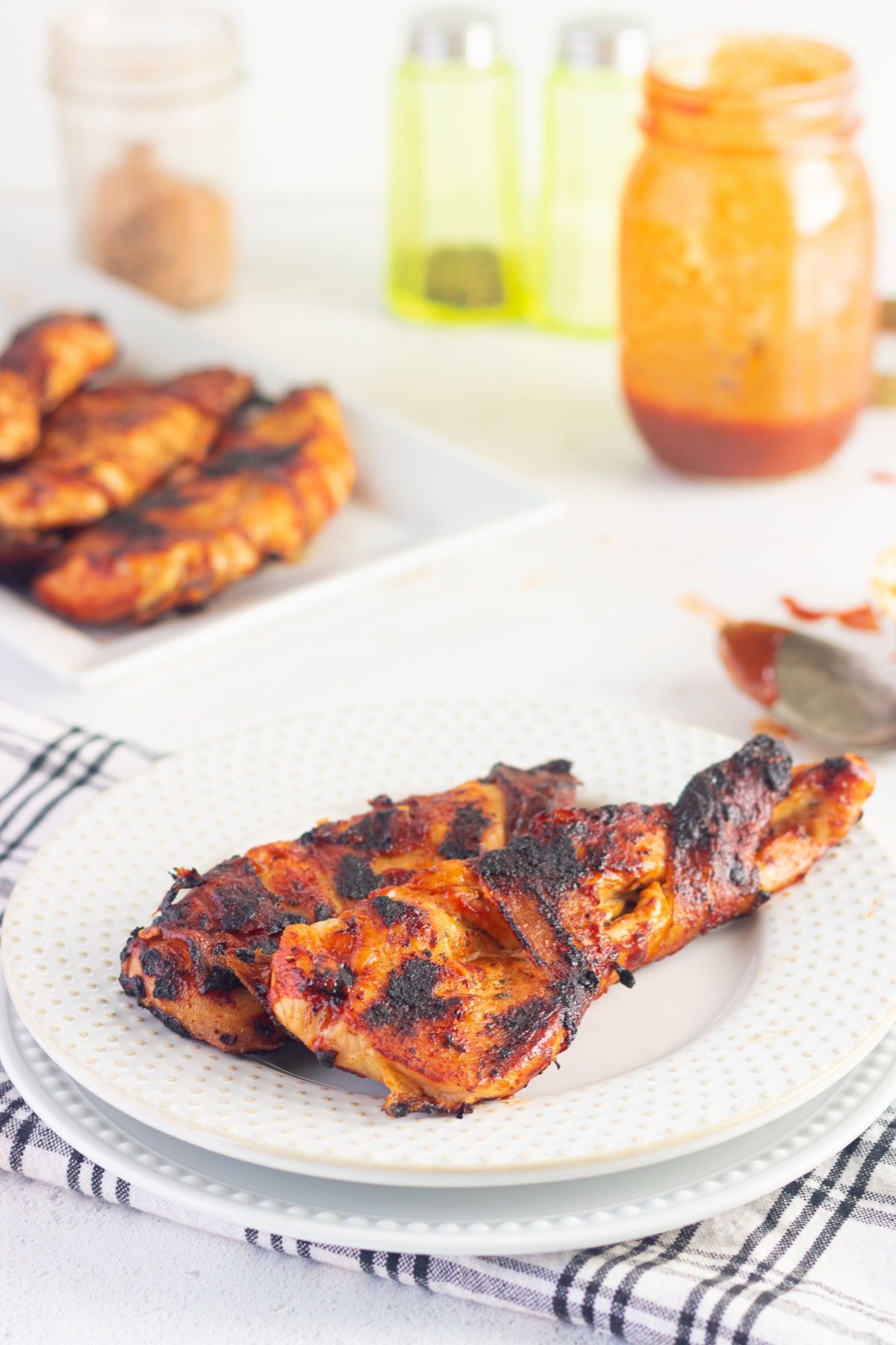 Bacon wrapped chicken breast, golden brown and juicy, on a table with a jar of barbecue sauce.