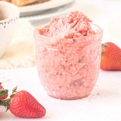 Closeup view of strawberry butter in a jelly jar with berries on the table beside it.