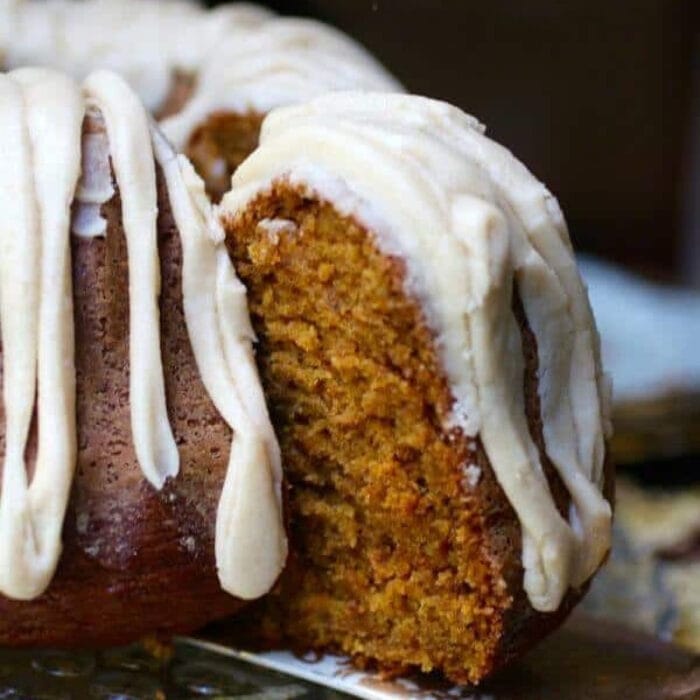 A slice of pumpkin spice bundt cake with white glaze being served.