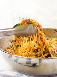 Tongs picking up a serving of taco spaghetti from the dish.