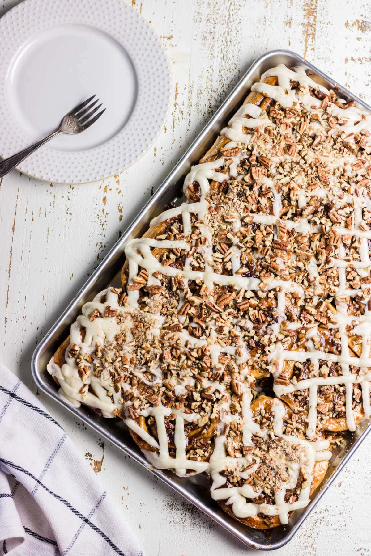 Overhead view of a full pan of pecan cinnamon rolls with frosting on top.