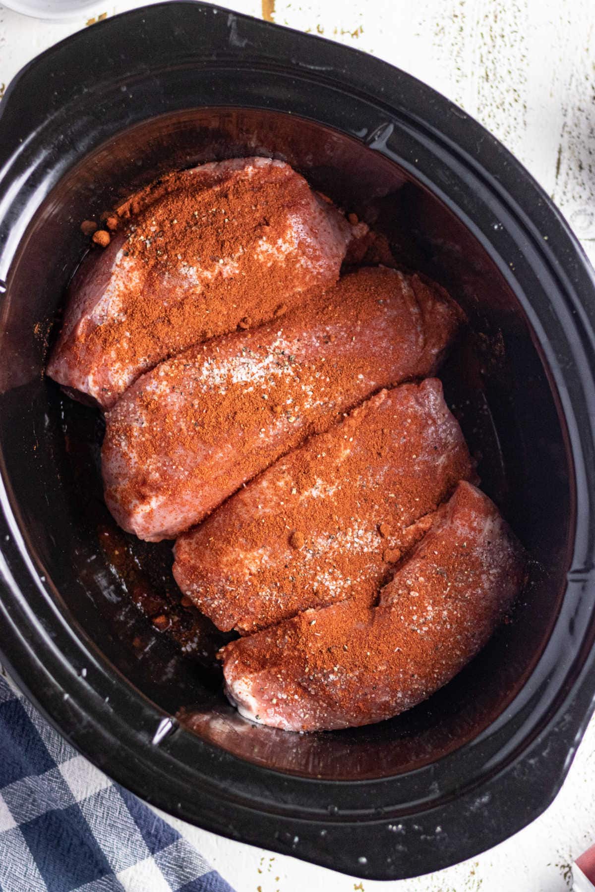 Image shows the pork being seasoned in the slow cooker.