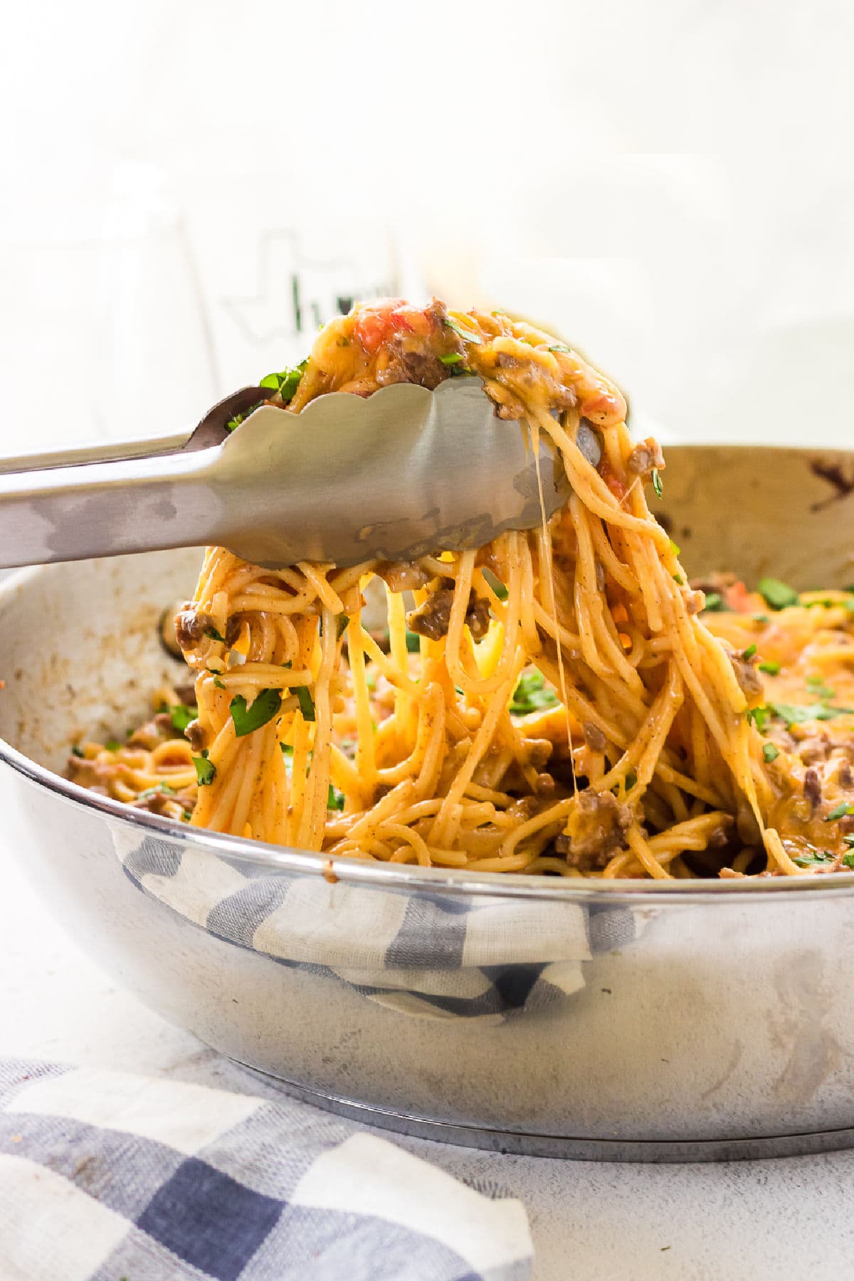 Tongs picking up a serving of taco spaghetti from the dish.