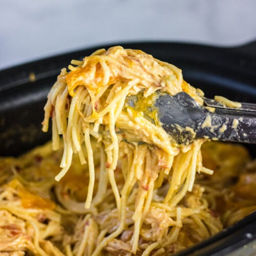 Tongs holding serving of pasta over slow cooker.