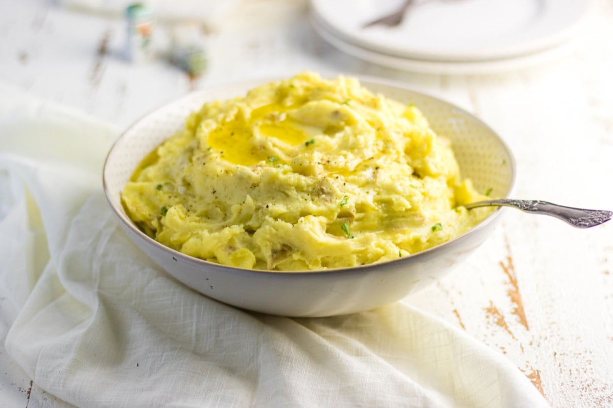 Serving bowl of potatoes with a spoon inside it.