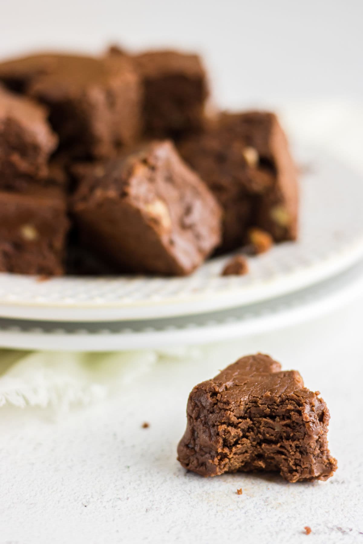 A piece of fudge with a bite taken out of it on the table. A plate of fudge is in the background.