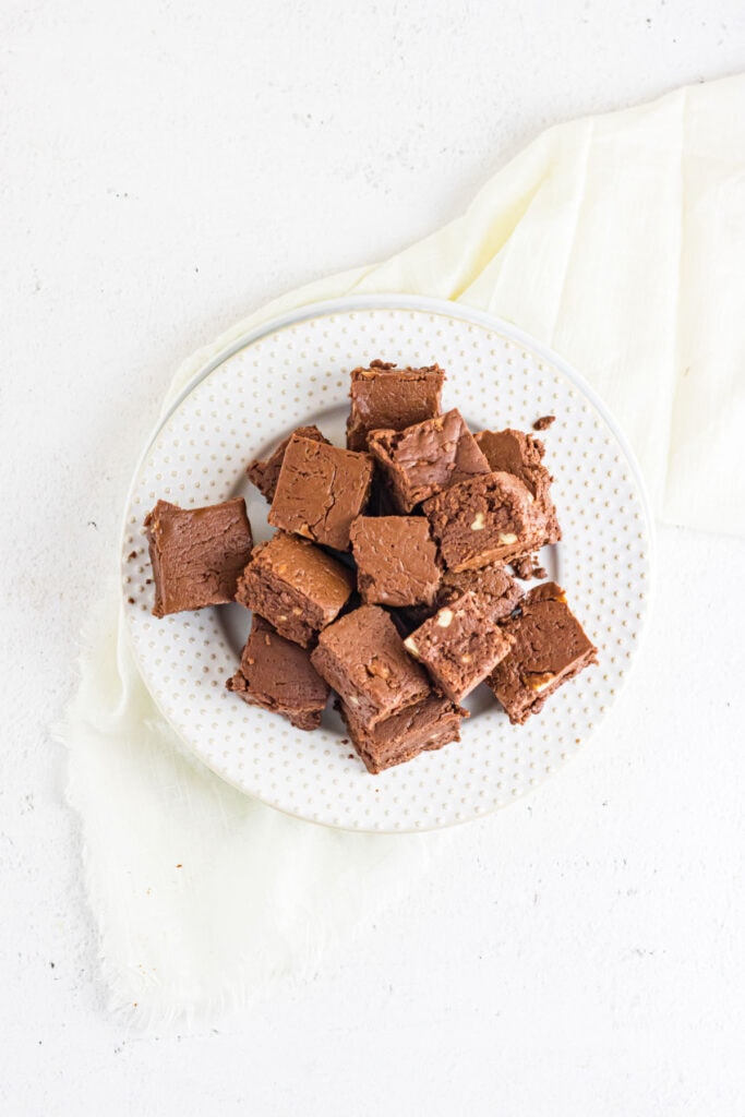 Overhead view of finished fudge squares stacked on a white plate on a beige napkin.