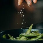 A hand sprinkling salt on vegetables. Text overlay for Pinterest.