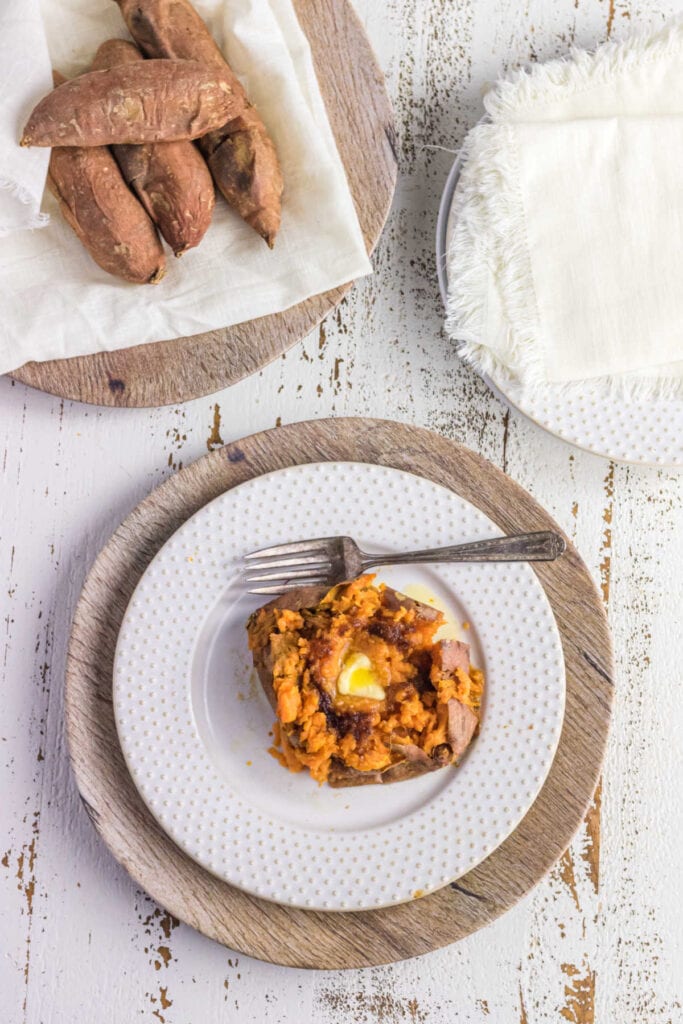 Overhead view of baked sweet potato on plate with more sweet potatoes on tray.