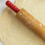 Rolling pin laying on a flat piece of pie dough with text overlay for Pinterest.