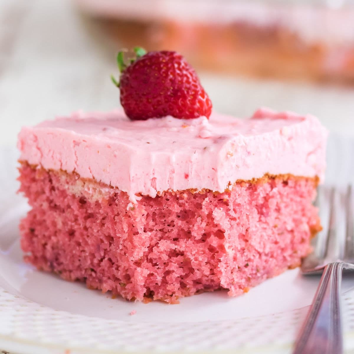Closeup of a square of strawberry cake with a berry on top.