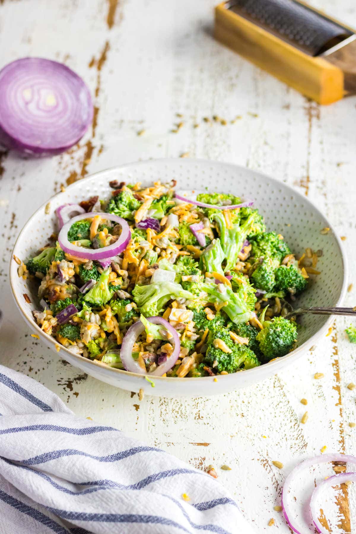 Keto broccoli salad in a white bowl with purple onions in the background.