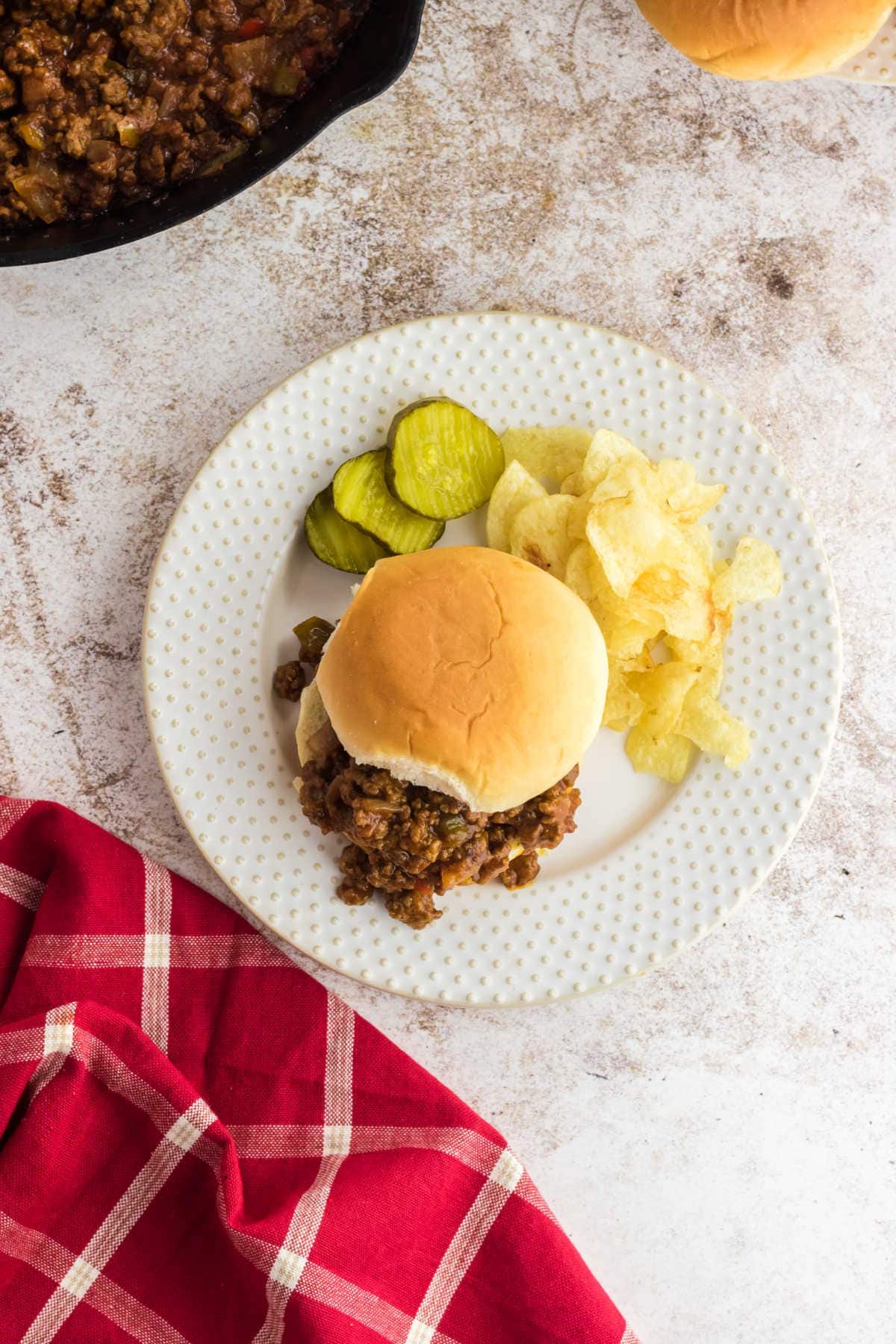 Overhead view of a sloppy joe sandwich on a plate with pickles.