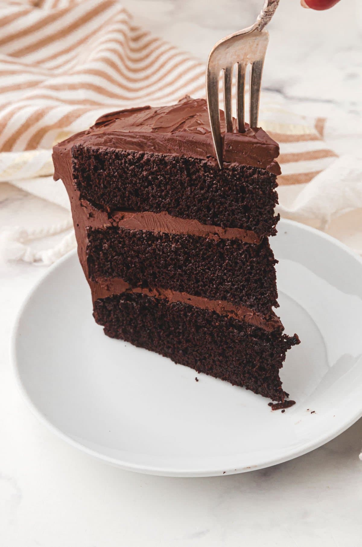 A slice of chocolate layer cake with a fork in it.