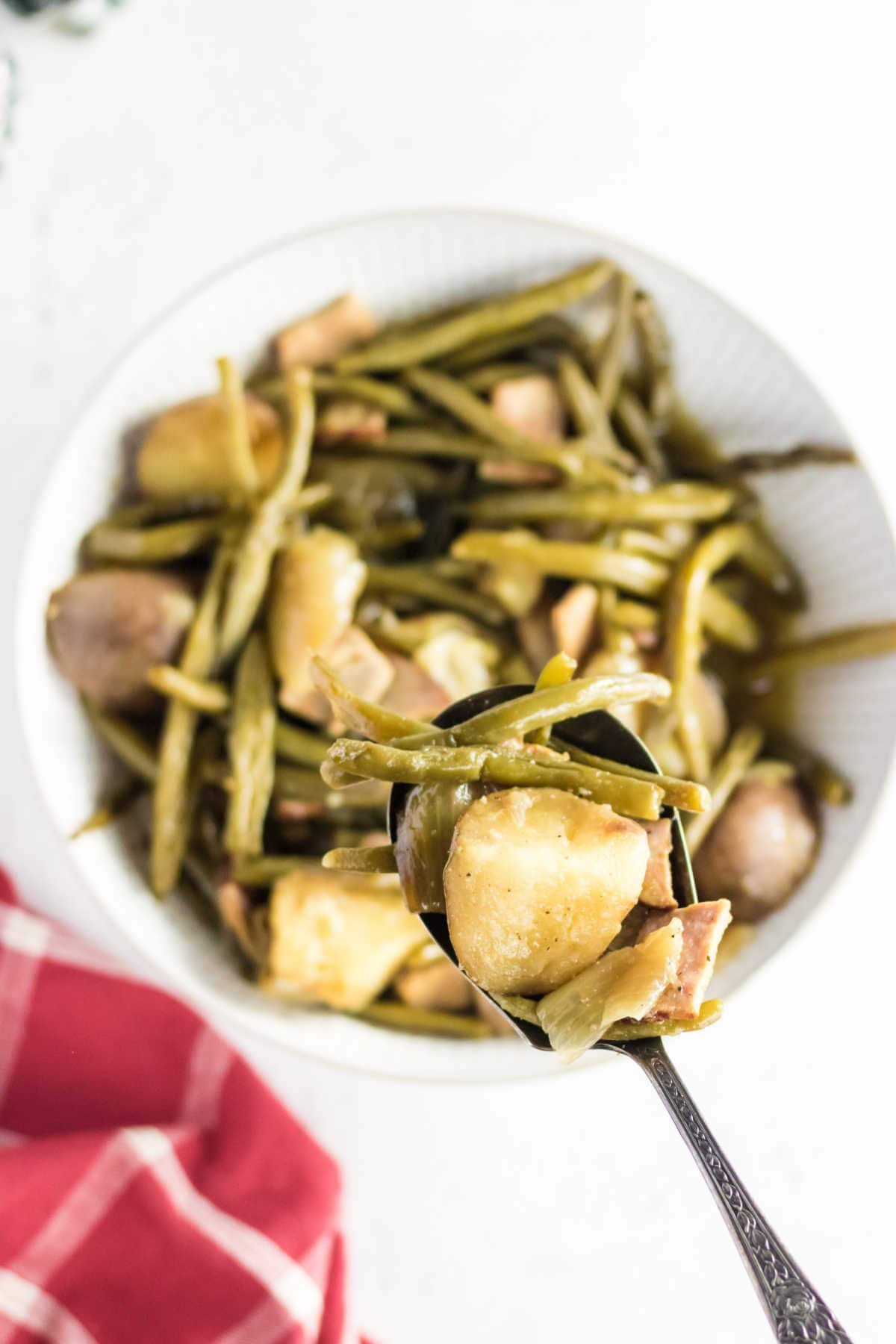 A serving spoon filled with green beans, ham, and potatoes.