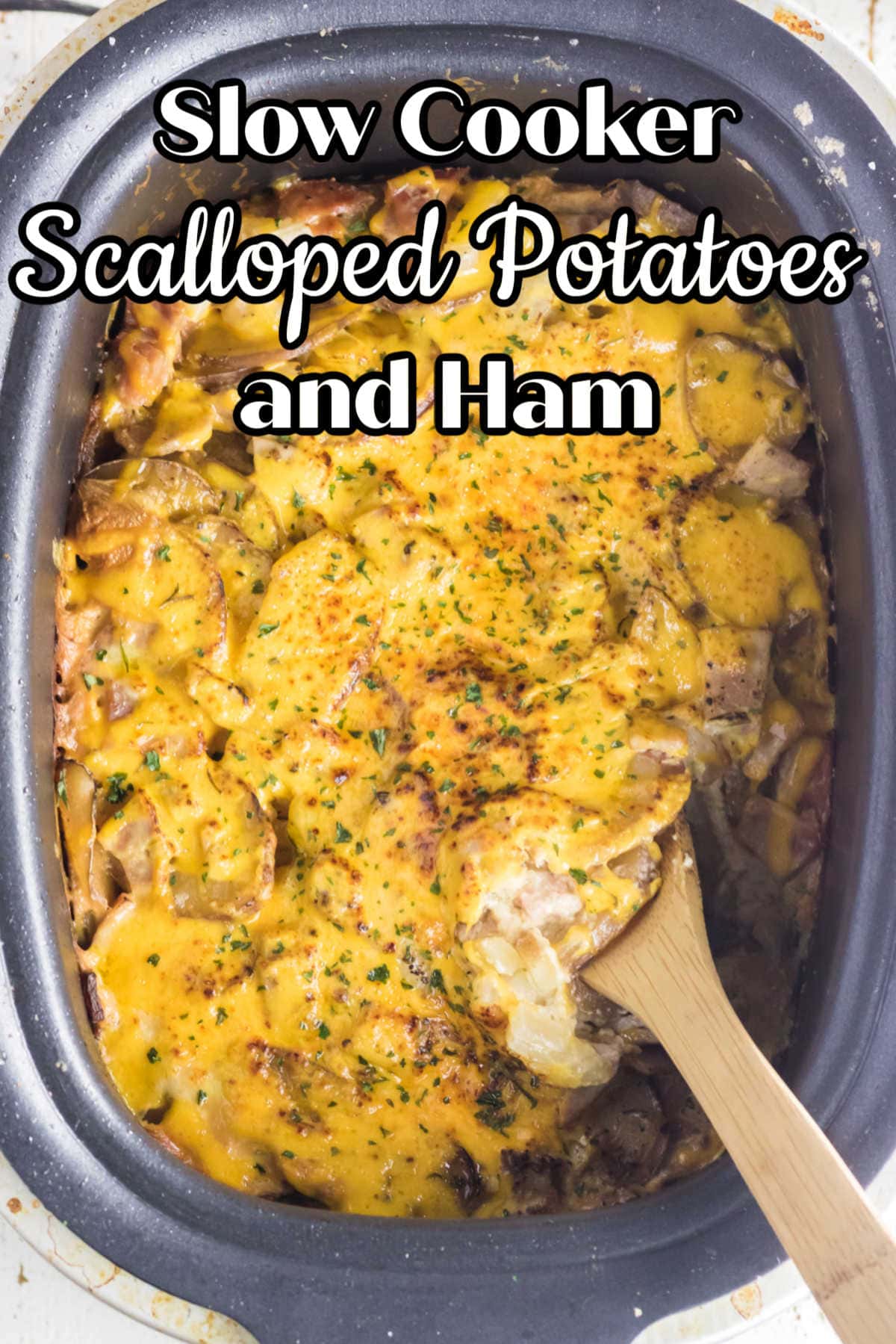 Scalloped potatoes in a slow cooker with a wooden spoon.