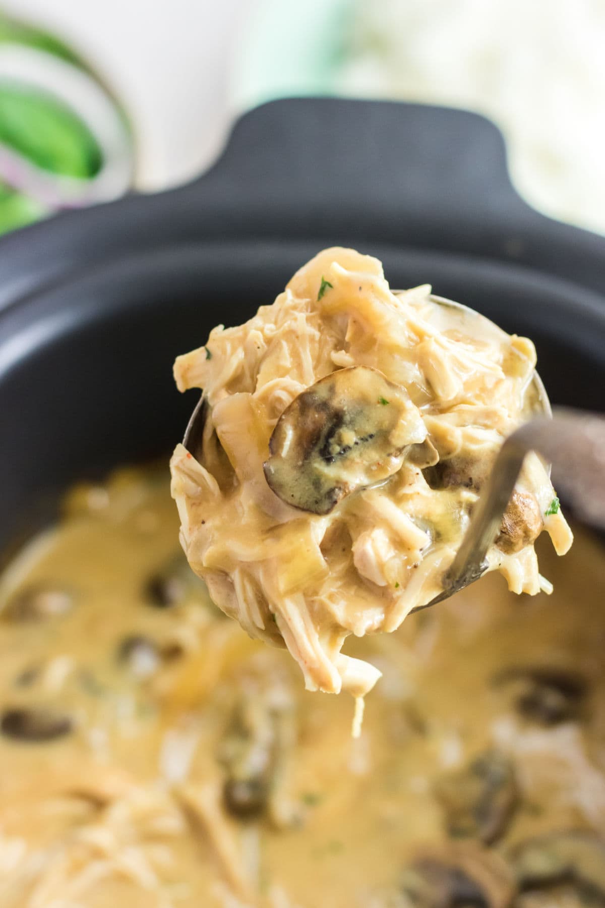 A ladle of creamy chicken being lifted from the crockpot.