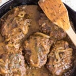 Overhead view of the hamburger steaks and gravy in an iron skillet with text overlay for Pinterest