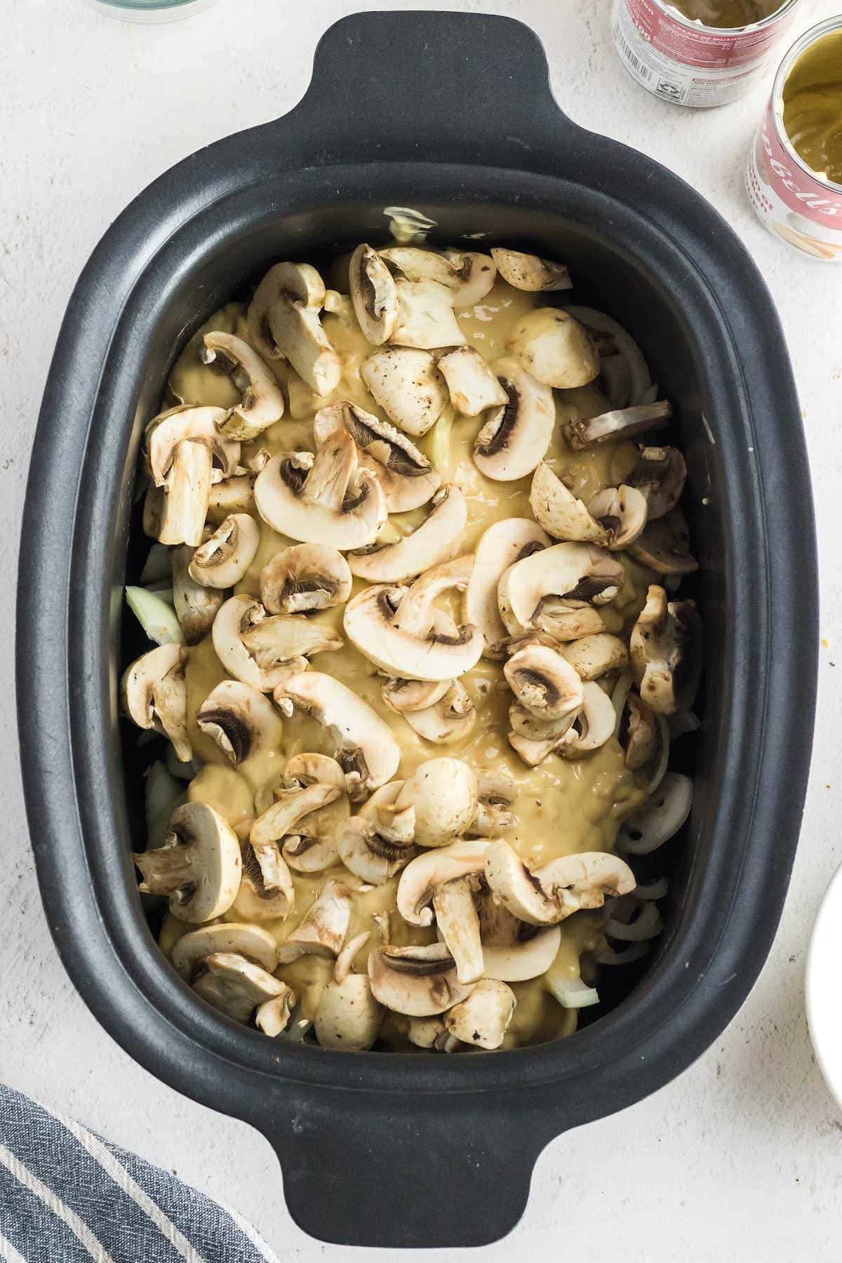Mushrooms have been sprinkled on top of the cream soup mixture and it's ready to cook.
