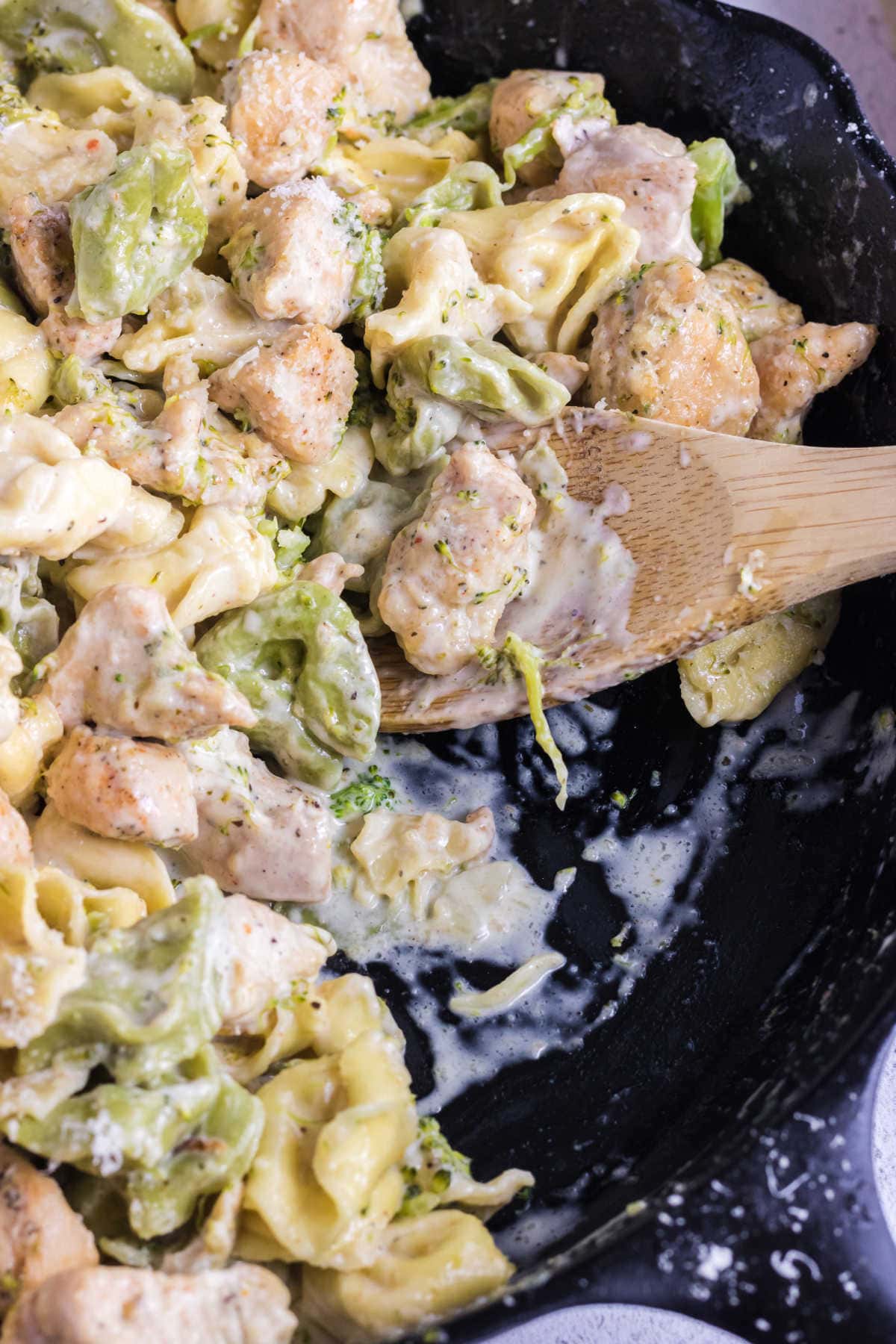 A pan of chicken tortellini alfredo with a wooden spoon in it.