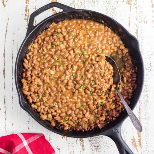 Overhead view of a skillet of baked beans with a spoon in it.