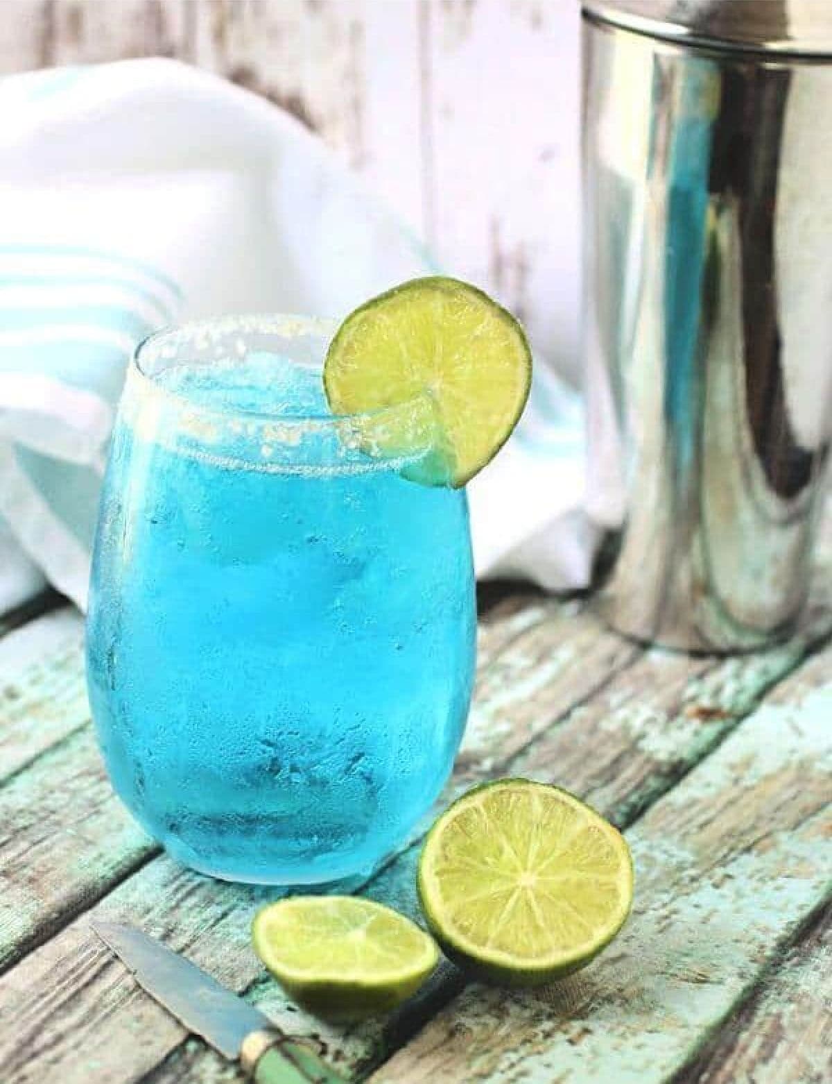 Blue cocktail with lime garnish on a table.