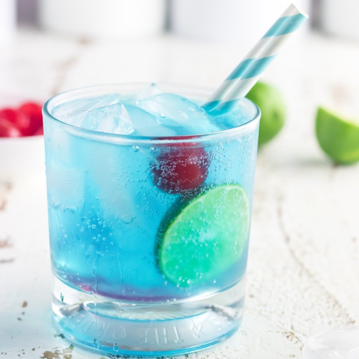 Closeup of a glass of gin and tonic with a cherry in it.